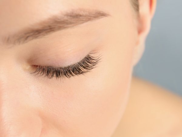 Young woman with beautiful long eyelashes on gray background, closeup. Extension procedure