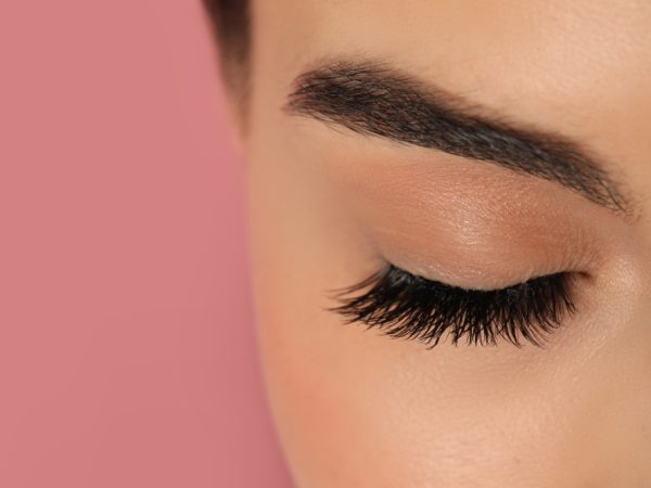 Beautiful young woman with long eyelashes on pink background, closeup. Space for text